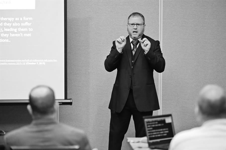  Kent Shafer signs at the front of a room during a workshop presentation.